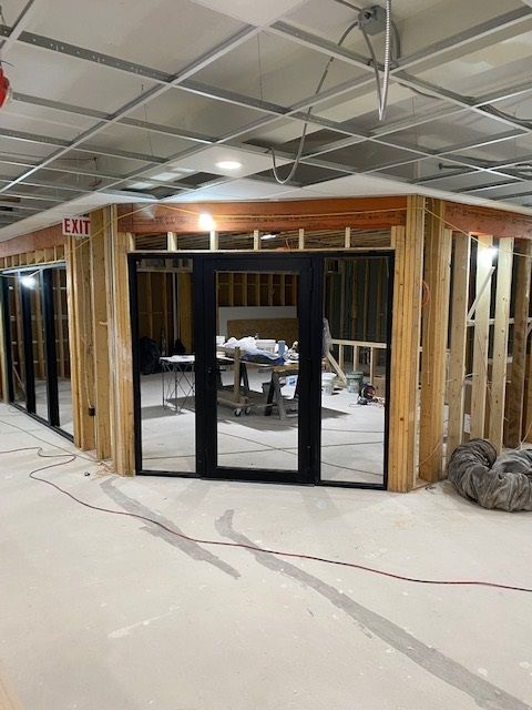 Interior construction of an office space with wood framing, black doors, and exposed ceiling grid.