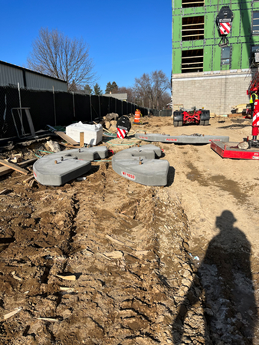 Construction site with gray concrete blocks, dirt, and a crane. Bright blue sky overhead.