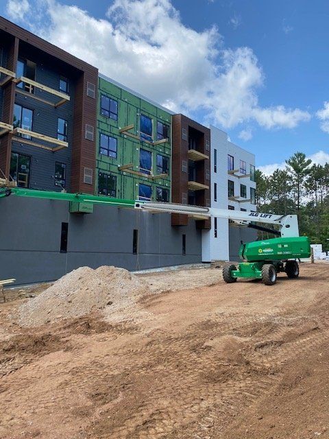 Multi-story building under construction with a lift on a dirt lot.