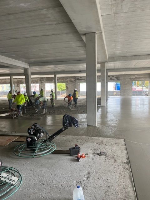 Construction site with workers smoothing wet concrete floor. Power trowel in foreground.