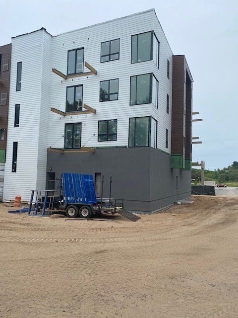 Multi-story building under construction; white siding, dark trim, blue trailer in front.