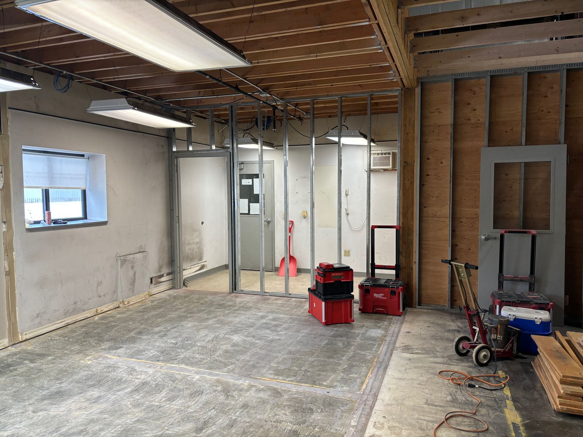 Interior view of a room under construction with metal studs, concrete floor, and tools.