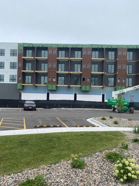 Building under construction with parking lot and green machinery; cloudy sky.