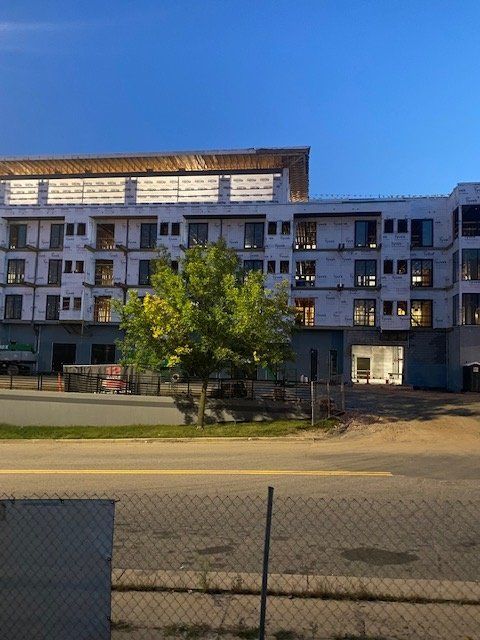 Multi-story building under construction with a tree in front. Evening setting with a blue sky.