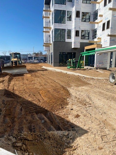 Construction site with bulldozer grading dirt near a multi-story building under construction; blue sky.