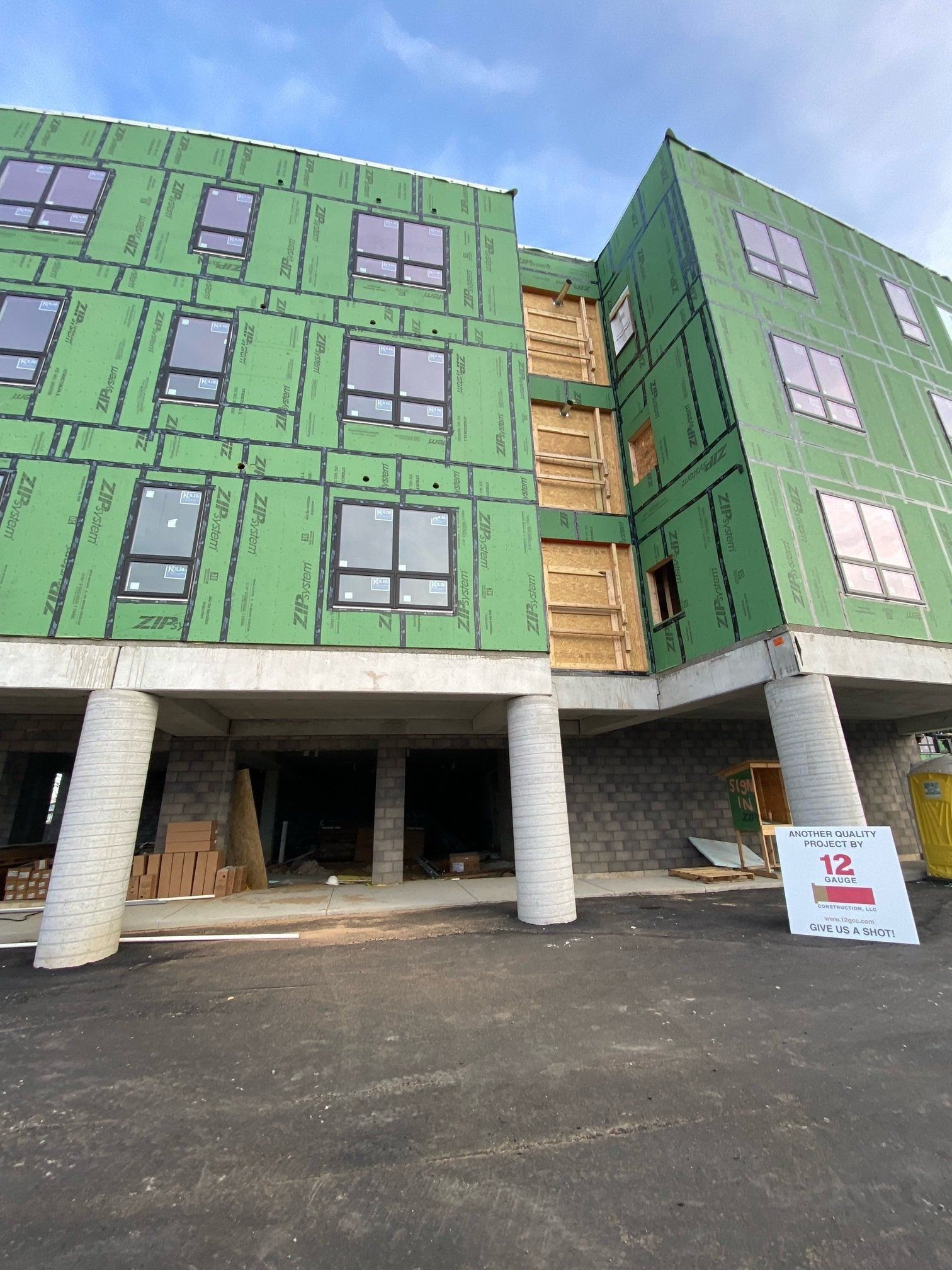Construction of a multi-story building with green siding and unfinished walls. Gray pillars support the structure.