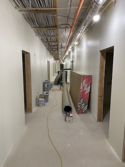 A long, empty hallway under construction; drywall, conduit, and other materials are present.