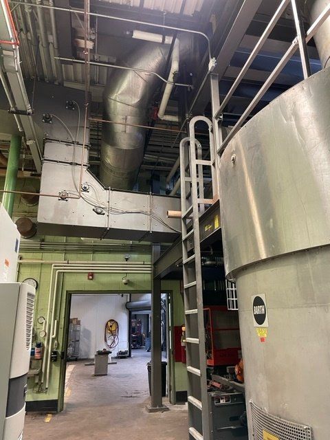 Industrial interior with large stainless steel tank, metal catwalk, and overhead ductwork.