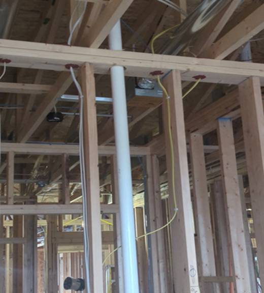Framing of a house under construction; white PVC pipe runs vertically through wooden beams; wires are visible.