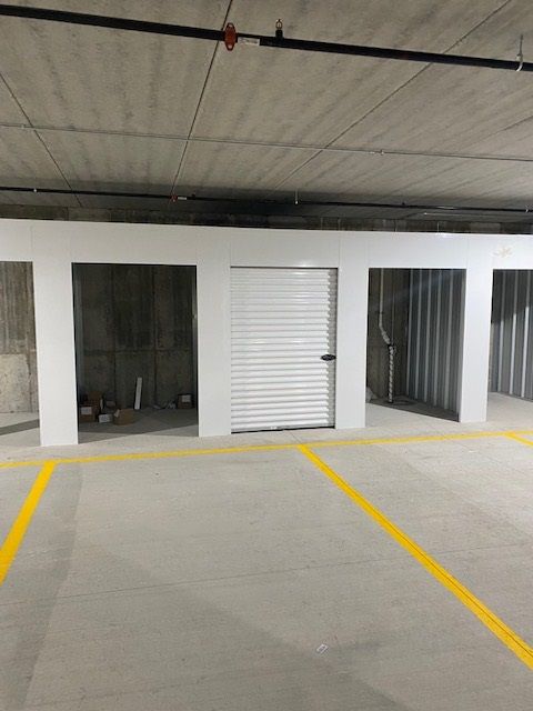 A row of storage units in a concrete parking garage, with yellow parking lines on the floor.