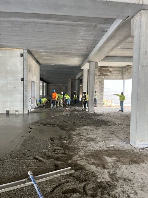 Construction workers leveling wet concrete floor in a building.