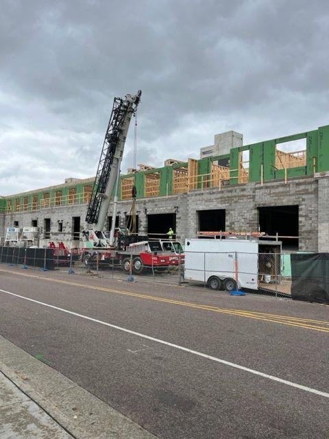 Construction site with crane, workers, unfinished building. Gray brick facade, wooden framing, cloudy sky.
