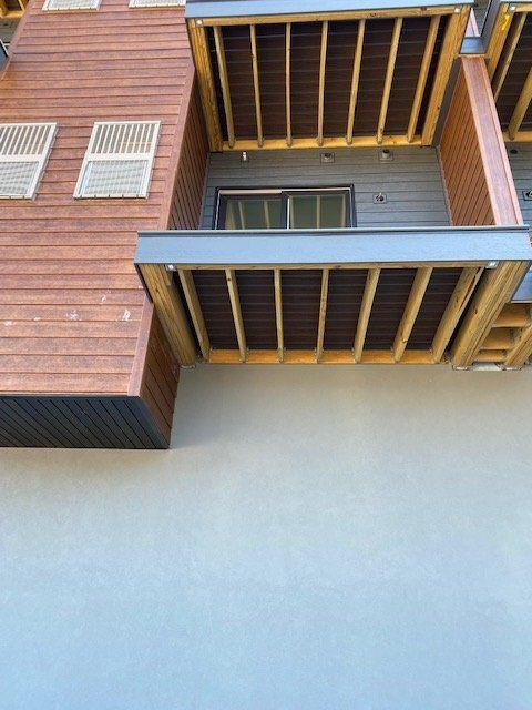 Exterior of a modern building with wooden and grey siding, balconies, and a light blue wall.
