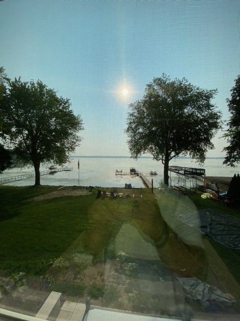 View of a lake with trees, a dock, and a bright sun.