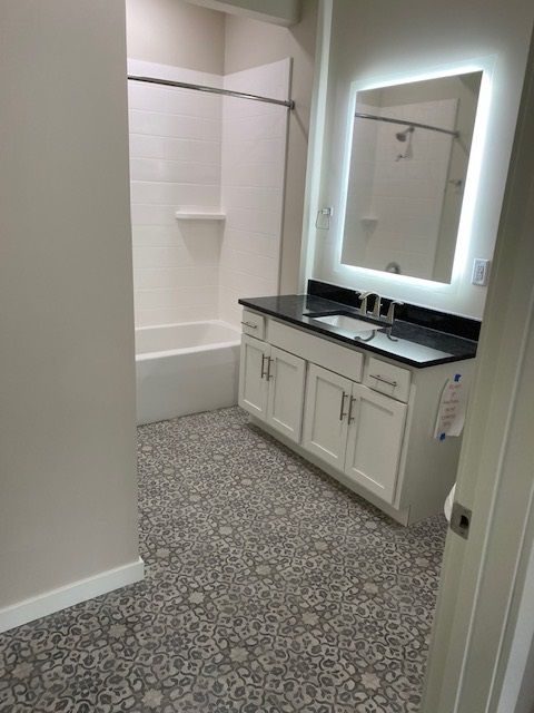 Bathroom with patterned floor, white vanity with black countertop, and a lit mirror.