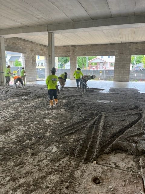 Construction workers spreading wet concrete on a large, open floor inside a building.