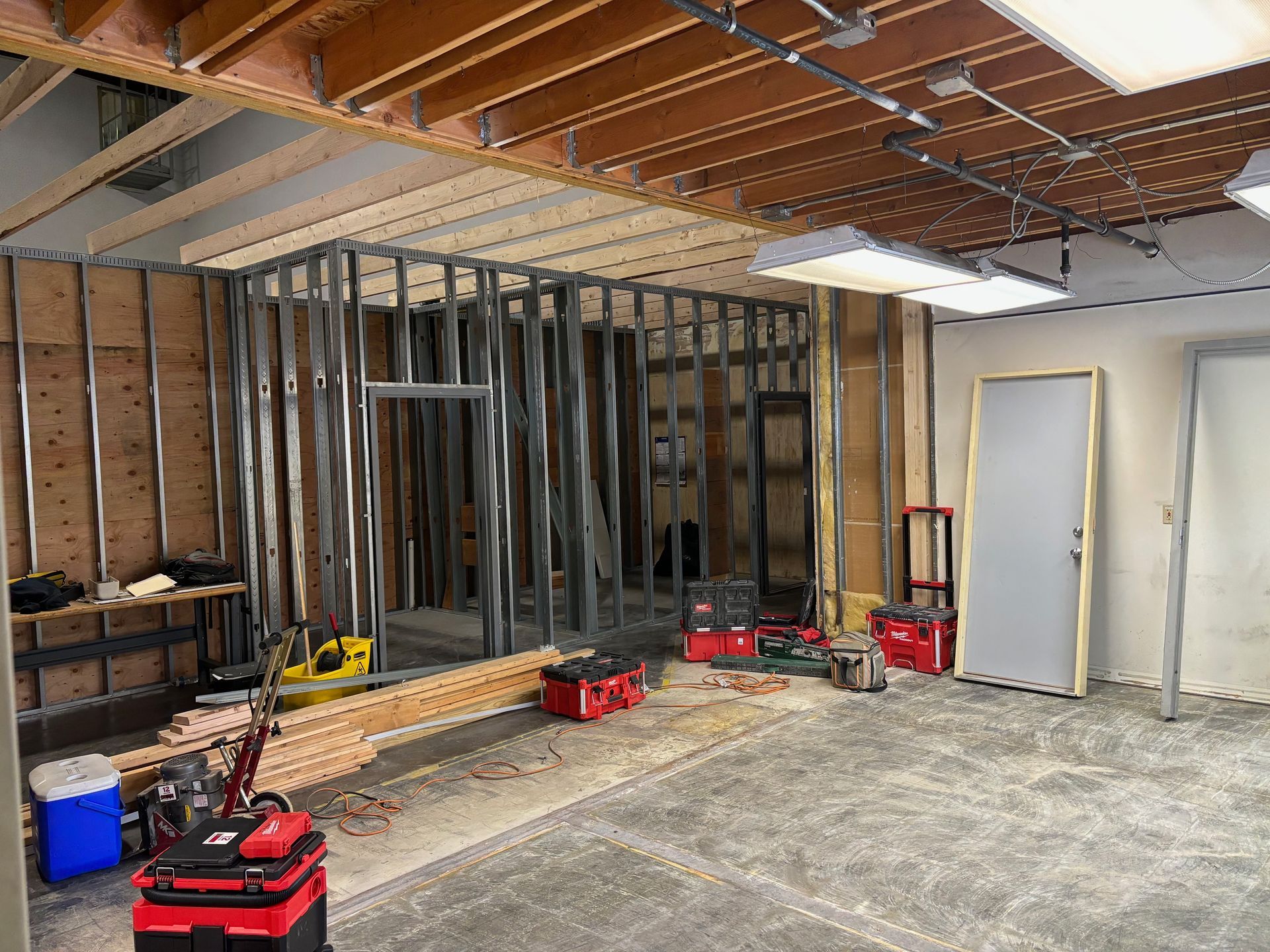 Interior construction site with metal studs, exposed wood, tools, and a door.