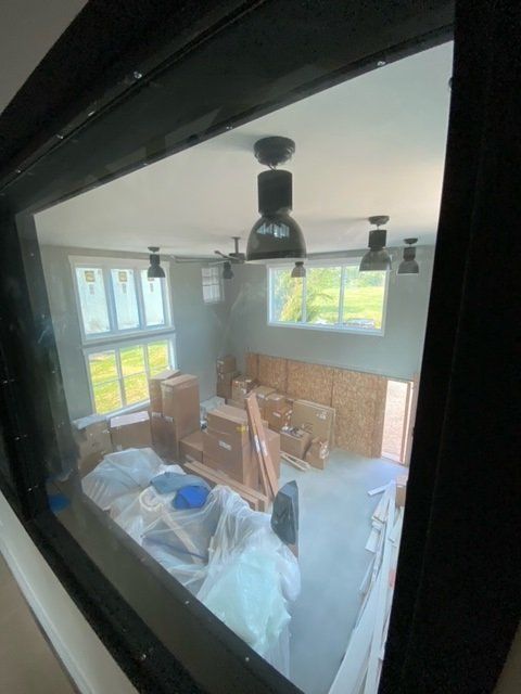 Interior room through a black-framed window. Construction materials and lights are visible inside.