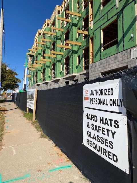 Construction site with black fencing and a sign requiring hard hats and safety glasses.