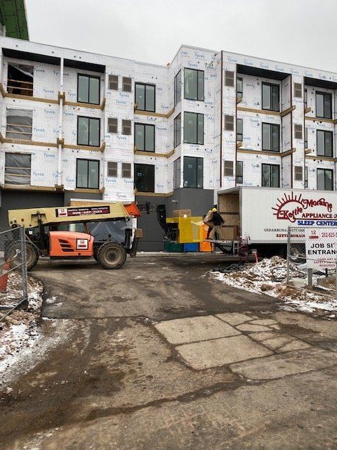 Construction site: lift, truck, workers, building exterior with windows, snow on the ground.