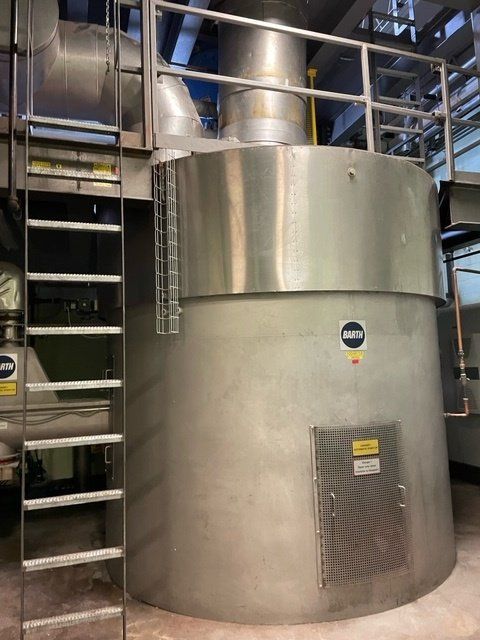 Large industrial metal tank with access ladder, ventilation, and piping in an industrial setting.