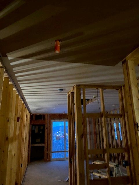 Interior of a building under construction, showing exposed wooden framing, metal ceiling, and a doorway with a window.