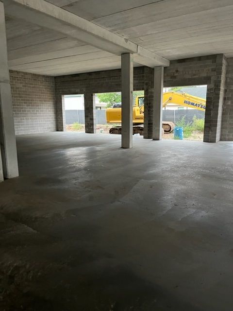 Interior of a concrete room with three open doorways, exterior view of an excavator.