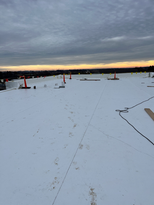 White flat roof with safety cones, footprints, and sunset sky.