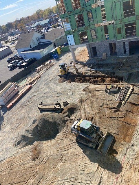 Construction site with heavy machinery like a backhoe and skid steer, building under construction.