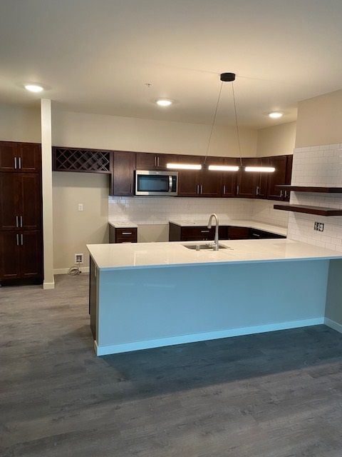 Modern kitchen with dark wood cabinets, white countertops, and a large island.