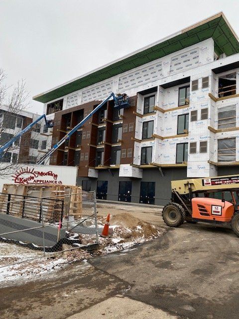 Construction site: multi-story building with workers in lifts, wood and white siding, cloudy sky.