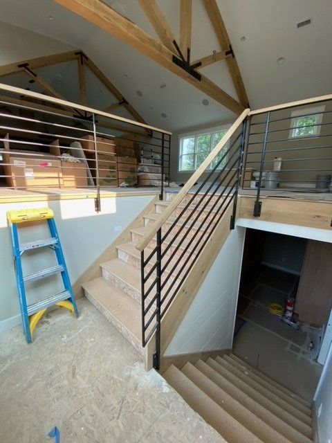 Staircase with horizontal black railings and wood steps. Blue ladder on the side. Interior view.