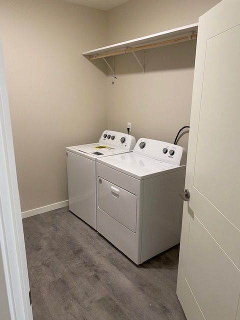 White washer and dryer in a laundry room with a shelf above. Gray floor, tan walls, open white door.