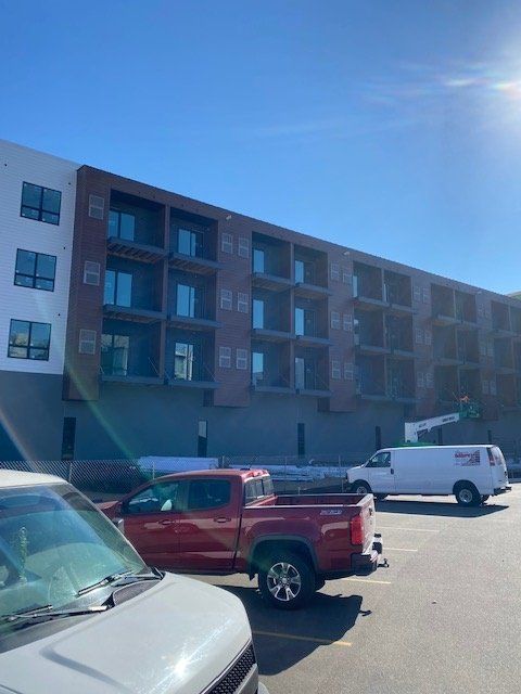 Apartment building under construction; red truck, white van parked in front, clear sky.