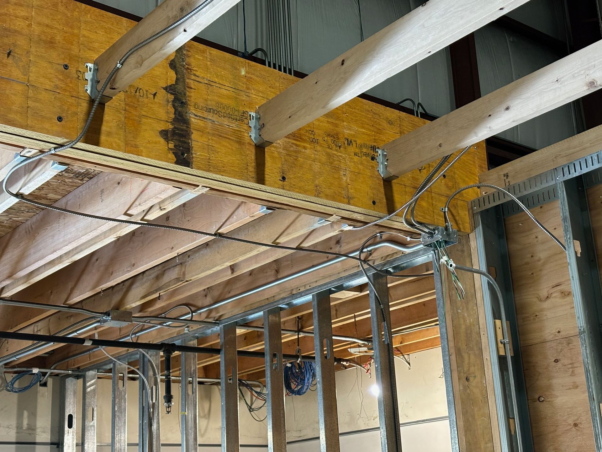 Exposed electrical wiring and wooden beams in a building under construction, with metal framing and plywood.