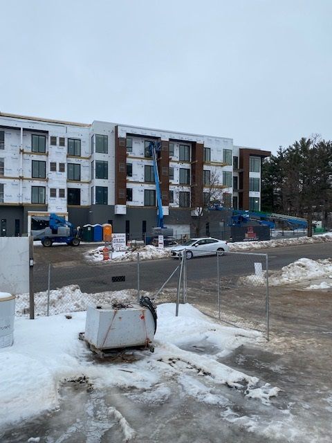 Construction of a multi-story building on a snowy day; workers use lifts; a white car parked on the street.