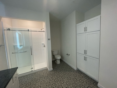 Bathroom with shower, toilet, and white cabinets against a patterned floor.