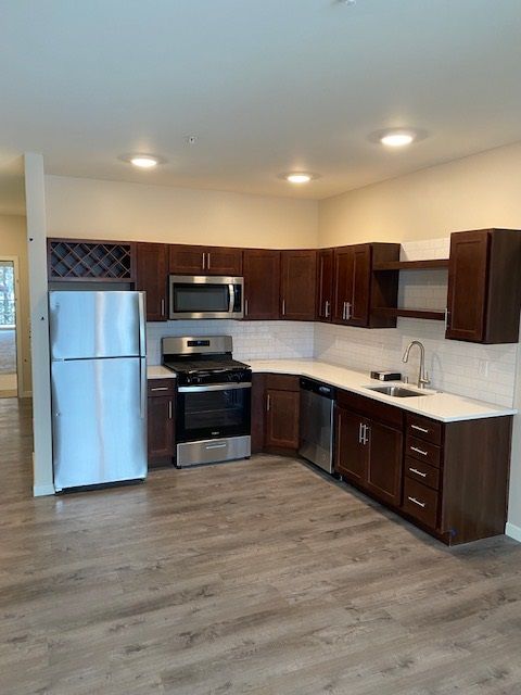 A kitchen with dark wood cabinets, stainless steel appliances, white countertops, and light wood-look flooring.