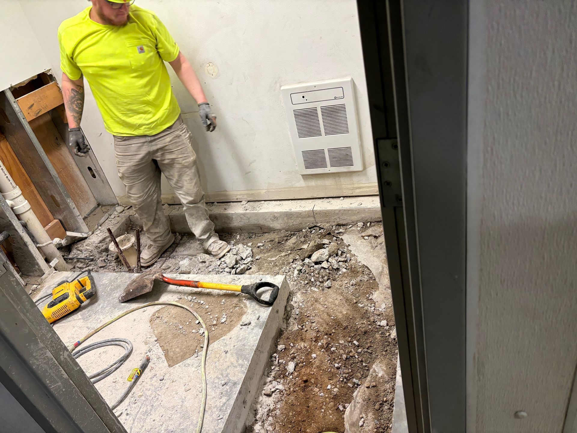 Construction worker in yellow shirt and tan pants breaking up flooring in a room.