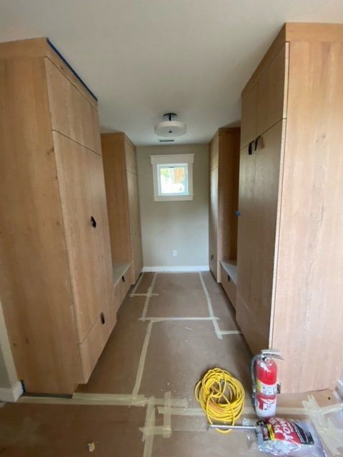 Narrow hallway with built-in wooden cabinets. A small window is in the center, with construction materials on the floor.
