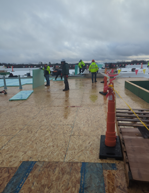 Construction workers on a rooftop, wearing safety vests, working under cloudy skies.