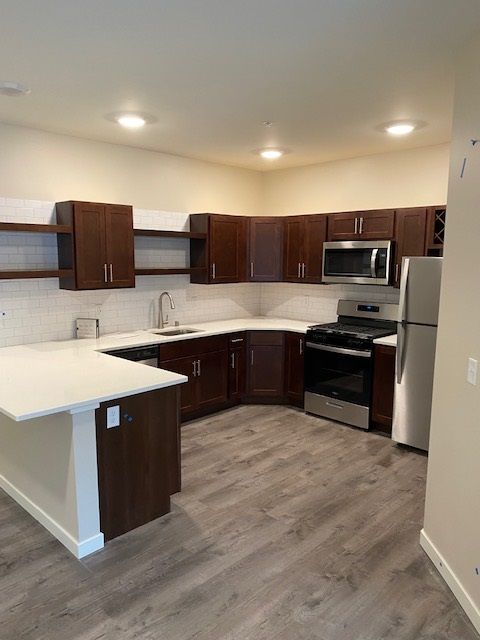 Modern kitchen with dark brown cabinets, white countertops, stainless steel appliances, and grey flooring.