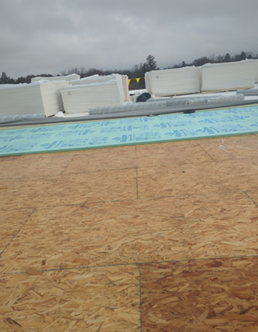 OSB sheathing, insulation, and roofing materials on a roof under overcast skies.