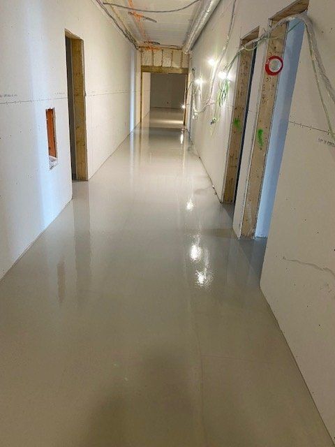 Long, empty hallway with a light-colored, glossy floor, unfinished walls, and doorways.