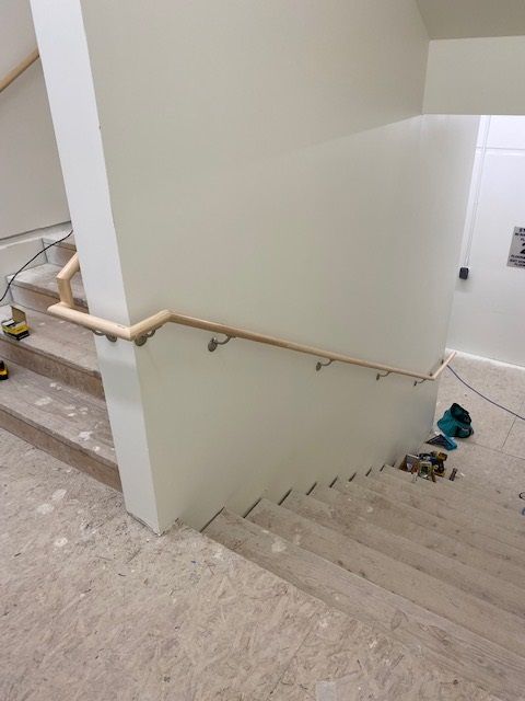 Staircase with wooden handrail being installed; unfinished steps and walls; tools on the floor.