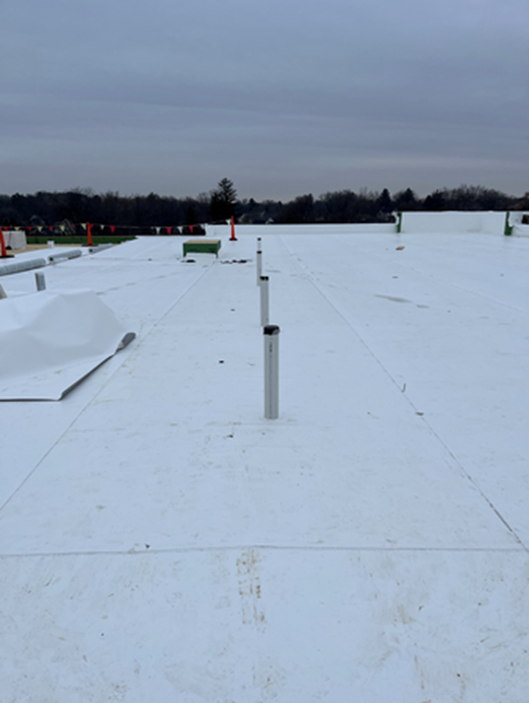 White commercial rooftop with vents under overcast sky.