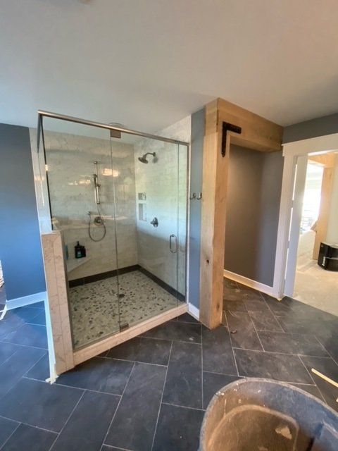 Shower stall with glass doors, stone tile floor, and wooden trim.