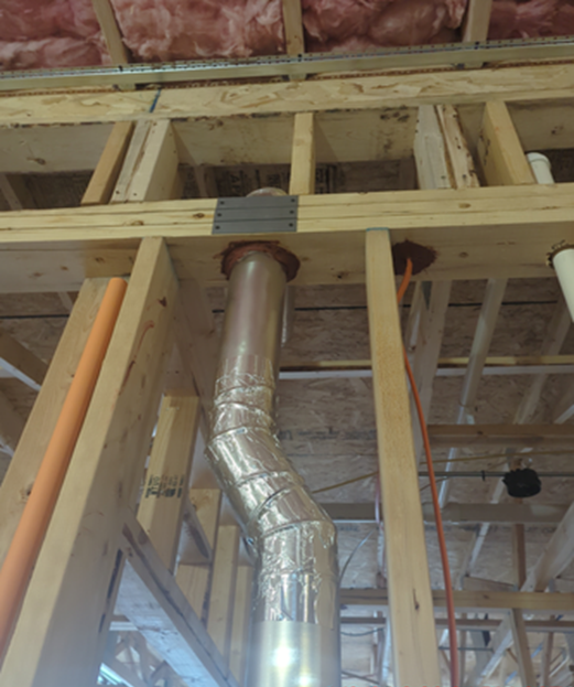 Framed wooden ceiling with a flexible metal ventilation duct passing through.
