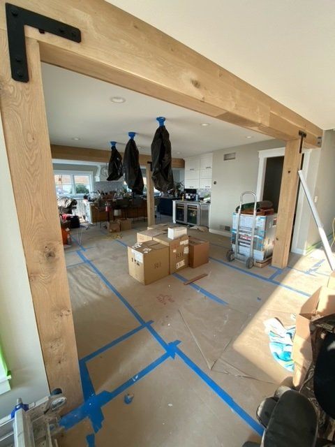 Interior view of a construction site with exposed wooden beams, tape on the floor, and unfinished areas.