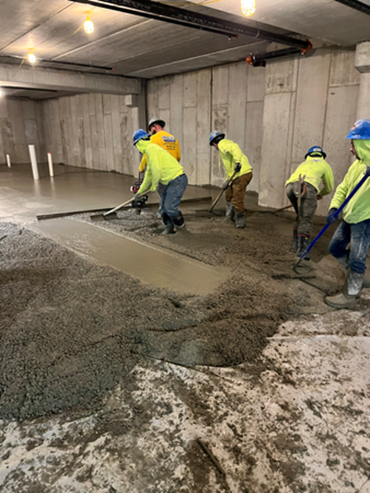 Construction workers smoothing wet concrete floor with tools in a concrete room.